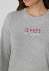 Sudadera gris con cuello redondo que presenta el texto "SLEEPY" en rosa y "state of mind" en blanco, hecha de suave material de algodón.