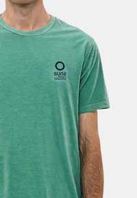 T-shirt di cotone verde con collo rotondo e maniche corte, con logo stampato nero "SUN2" e testo sul lato sinistro del petto.