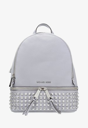 Sac à dos Michael Kors en cuir gris clair avec des clous pyramidaux argentés sur la moitié inférieure et deux curseurs de fermeture éclair sur la poche avant.