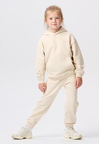 Beige Kapuzenpullover- und Jogginghosen-Set aus weichem Material. Der Kapuzenpullover hat eine vordere Tasche, während die Hose elastische Bündchen hat.