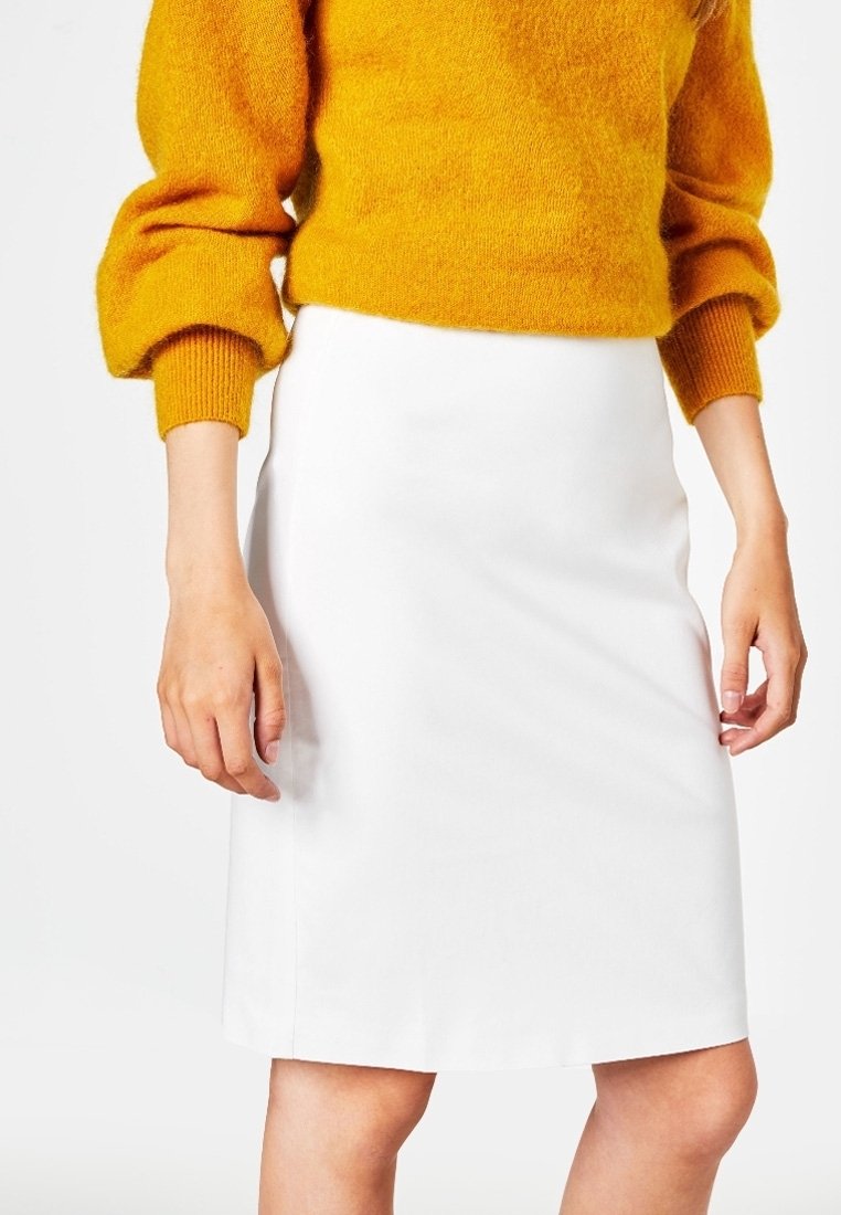 Jupe blanche jusqu'aux genoux avec une texture lisse, associée à un pull jaune vif texturé avec des manches ballon.