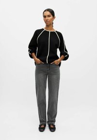 Maglione nero con piping bianco, maniche oversize; abbinato a jeans grigi a gamba larga e scarpe basse nere. Design semplice e moderno.