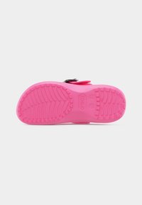 Ροζ σόλα σανδάλου Crocs που δείχνει υφή πέλματος με ανάγλυφο σχέδιο και λογότυπο, σε απλό φωτεινό φόντο.