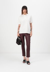 Bela polo majica kratkih rukava opuštenog kroja, u kombinaciji s prilagođenim burgundy hlačama od umjetne kože i crnim sandalama otvorenih prstiju. Drži crnu torbicu.