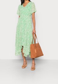 Ljusgrön blommig klänning med korta ärmar och en hög-låg fåll, i kombination med en beige mockaväska och beige höga sandaler.