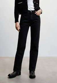 Jean en denim noir avec une coupe droite, taille haute et design classique à cinq poches, associé à des bottes de cheville noires.