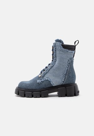 Blue denim combat boot with frayed edges, black chunky sole, black pull tab, and metal eyelets for laces on a white background.