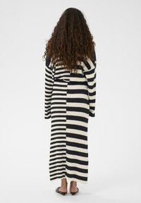 Ribota, garām piedurknēm, kleita melnbaltā svītrā, ar brīvu siluetu un sānu izgriezumiem, kas nodrošina vieglu kustību, ar teksturētu apdari.