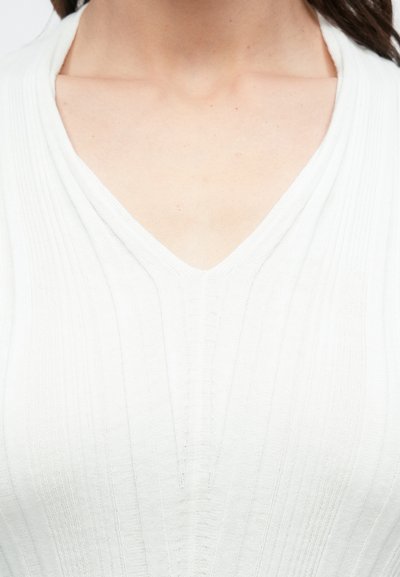 Λευκό, ριμπ πλεκτό τοπ με V-λαιμόκοψη, που διαθέτει κάθετες υφασμάτινες γραμμές και λεία επιφάνεια, εστιάζοντας στην απλότητα και την κομψότητα.