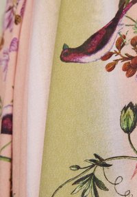 Lähivõte lillemustrist, kus on prinditud roosi- ja lillakaid linde ning rohelisi lehti pastellrohelisel ja -roosal taustal.
