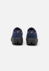 Navy suede hiking shoes with black rubber outsole, featuring a padded collar, brand logo on heel, and textured tread for traction.