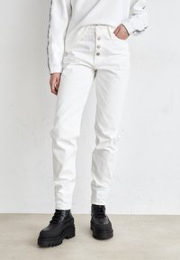 Bílé džínové kalhoty s vysokým pasem, s pěti knoflíky a slim fit střihem, s lehkým texturovým detailem, spojené s robustními černými kotníkovými botami.