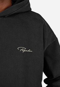 Czarna bawełniana bluza z kapturem z napisem "Pegador" w kolorze kremowym. Materiał ma miękką teksturę, luźny krój oraz duży kaptur.