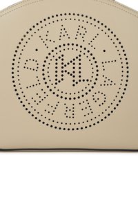 Beige ādas virsma ar perforētu apļveida dizainu, kurā iekļauti teksta un emblēmu detaļas, papildināta ar melnu apmali pa malas.