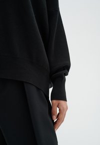 Black knitted sweater with a loose fit and dropped shoulders. Features ribbed cuffs and a soft texture, paired with black trousers.