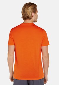 Herreskjorte med korte ærmer i lys orange, lavet af blødt stof, rund hals, glat tekstur og lige kant. Har en logoetiket på siden.