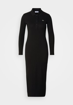 Czarna, prążkowana sukienka polo z długim rękawem o dopasowanej sylwetce. Posiada klasyczny kołnierzyk oraz małe, zielone haftowane logo na klatce piersiowej.