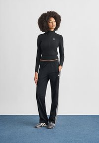 Black zip-up athletic jacket with a fitted design and an Adidas logo, paired with black track pants featuring white side stripes.