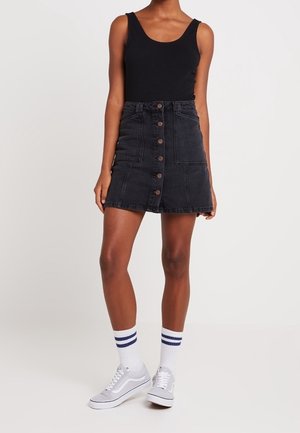 Black denim skirt with front buttons, mid-thigh length, paired with a black tank top and gray sneakers, featuring striped socks.