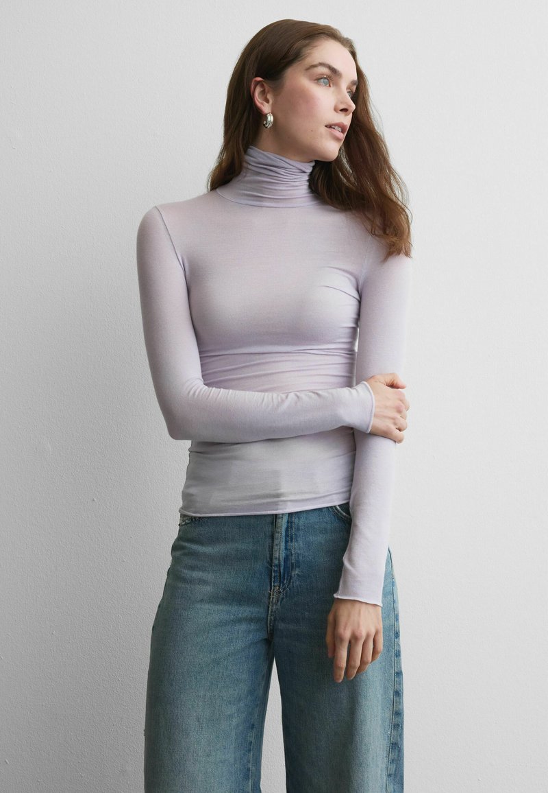 Haut à col roulé manches longues de couleur violet clair, au design ajusté, associé à un jean en denim taille haute. Texture lisse sans motifs visibles.