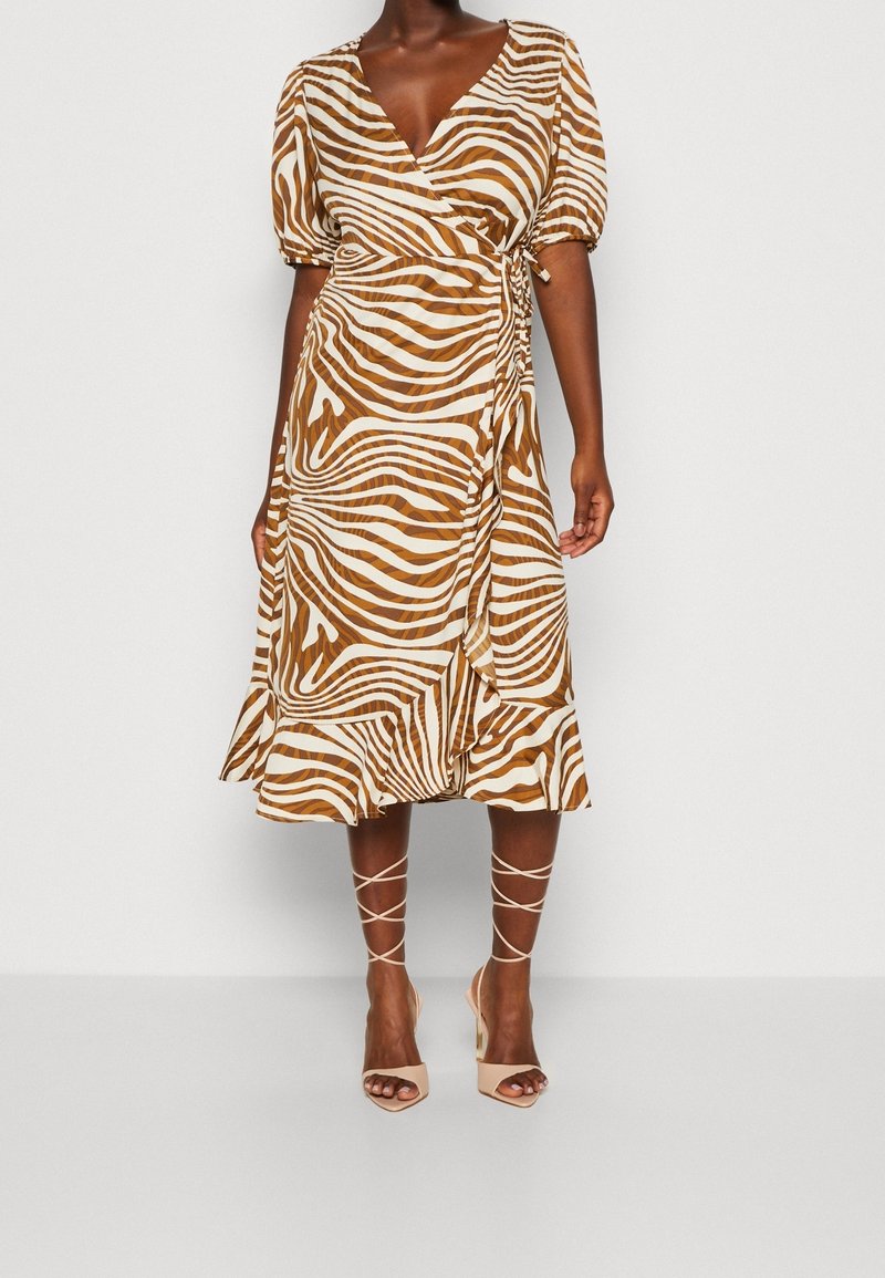 Femme portant une robe portefeuille marron et blanche à imprimé zèbre avec manches bouffantes et ourlet volanté, associée à des talons beiges à lacets.