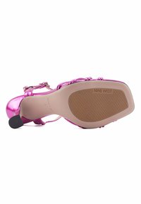 Sandal con tacco in pelle verniciata rosa, con dettagli della fascia e fibbia, caratterizzata da una suola liscia con texture a coste e logo del marchio sul fondo.