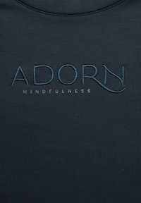 Dunkelblauer, strukturierten Stoff mit gesticktem Text: "ADORN" in Türkis und "MINDFULNESS" in einer helleren Farbe darunter.