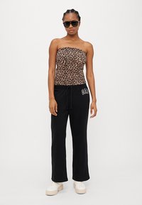 Top sem mangas de padrão de leopardo, calças de moletom pretas com cordão e logo na perna, combinadas com sapatilhas brancas de plataforma e óculos de sol escuros.