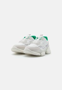 Białe buty sportowe z zielonymi akcentami, wykonane z siateczki i zamszu, z teksturowaną podeszwą i wyściełanym kołnierzem dla komfortu.