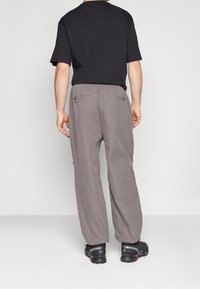 Šedé volné kalhoty s elastickým pasem, dvěma zadními kapsami a jemnými detaily švů. V kombinaci s černým tričkem s krátkým rukávem a černými botami.