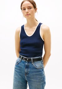 Marinblå ribbad linne med vita detaljer, med djup V-ringning och figursydd design, ihop med högmidjade ljusblå denimjeans.