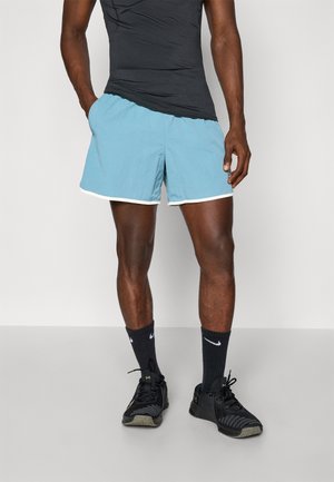 Helle blaue Badeshorts mit weißen Akzenten, die einen lockeren Schnitt und eine weiche Textur haben, kombiniert mit schwarzen Sportschuhen und dunklen Socken.