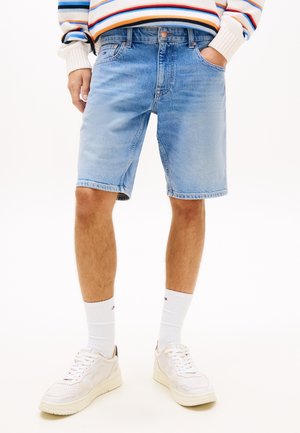 Mand iført lyseblå denimshorts, hvide sokker, hvide sneakers og en cremefarvet sweater med farverige striber.