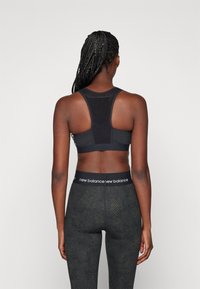 Sutiã desportivo preto com design racerback e painéis em malha, combinado com leggings pretas com um padrão texturizado e uma cinta com marca.