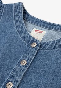 Chemise en denim bleu clair avec un col rond, une fermeture à boutons avec des accessoires argentés, et un tissu doux et texturé. Étiquette Levi's visible.