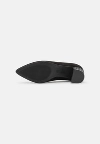 Scarpa nera in suede con tacco alto, punta appuntita e suola testurizzata; presenta un tacco basso nero con un accentuato motivo sul retro.