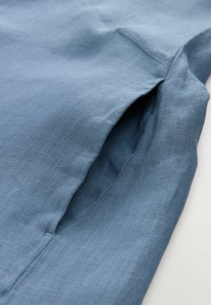 Tessuto blu chiaro con una finitura liscia e testurizzata. Presenta una piccola tasca angolata e cuciture sottili. Materiale morbido e leggero.