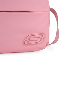 Bolso de hombro de nailon rosa con una textura suave, que presenta un bolsillo con cremallera y un acento de logo elevado en la parte delantera.