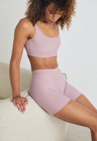 Set di reggiseno sportivo e pantaloncini color rosa chiaro realizzato in tessuto elastico, caratterizzato da una texture liscia e un design minimalista. Senza logo prominente.