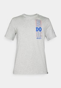 Vaaleanharmaa lyhythihainen T-paita, jossa on pystysuoraan sinisellä ja punaisella ympäröity teksti "JUST DO IT." ja pieni "ATLETI" vasemmalla rinnalla.