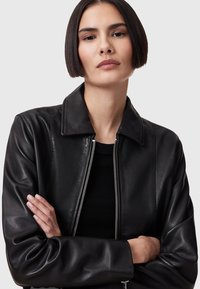 Chaqueta de cuero negro con cierre de cremallera, cuello plano y mangas largas. Textura suave con un ligero brillo. Diseño simple y ajustado para un estilo moderno.