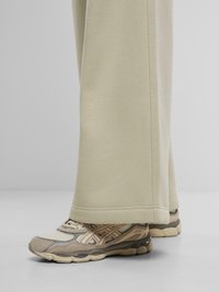 Pantalons de survêtement beige clair à jambes larges, associés à des chaussures de sport beige et gris avec des accents en maille et en caoutchouc.