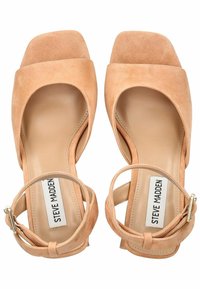 Sandalias de tacón alto de ante beige con punta cuadrada, correa para el tobillo y plantilla acolchada. La etiqueta de la marca es visible en la plantilla.