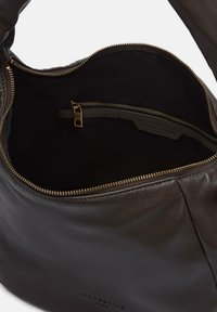 Braune Ledertasche mit einer glatten Textur und Reißverschluss in Goldfarbe. Das Innere verfügt über ein schwarzes Stofffutter und eine Reißverschlusstasche zur Organisation.