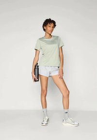 Hele roheline lühikeste varrukatega spordipolt, kombineeritud hallide lühikeste püksidega. Mudel hoiab musta veepudelit. Kaasas hallid põlvesokid ja jooksujalatseid.