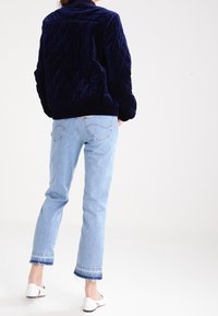 Giacca trapuntata in velluto blu navy con colletto alto, orlo a coste e tasche laterali, abbinata a jeans croppati azzurri con orli sfrangiati.
