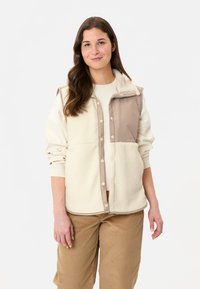 Gilet doublé en polaire, en crème et taupe, avec un devant boutonné, un col montant et des sections de tissu contrastées pour la texture et l'intérêt visuel.