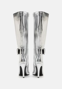 Stříbrné kozačky ke kolenům s lesklým kovovým povrchem, vybavené špičatou špičkou, lodičkovým podpatkem a páskem se sponou pro bezpečné upevnění.