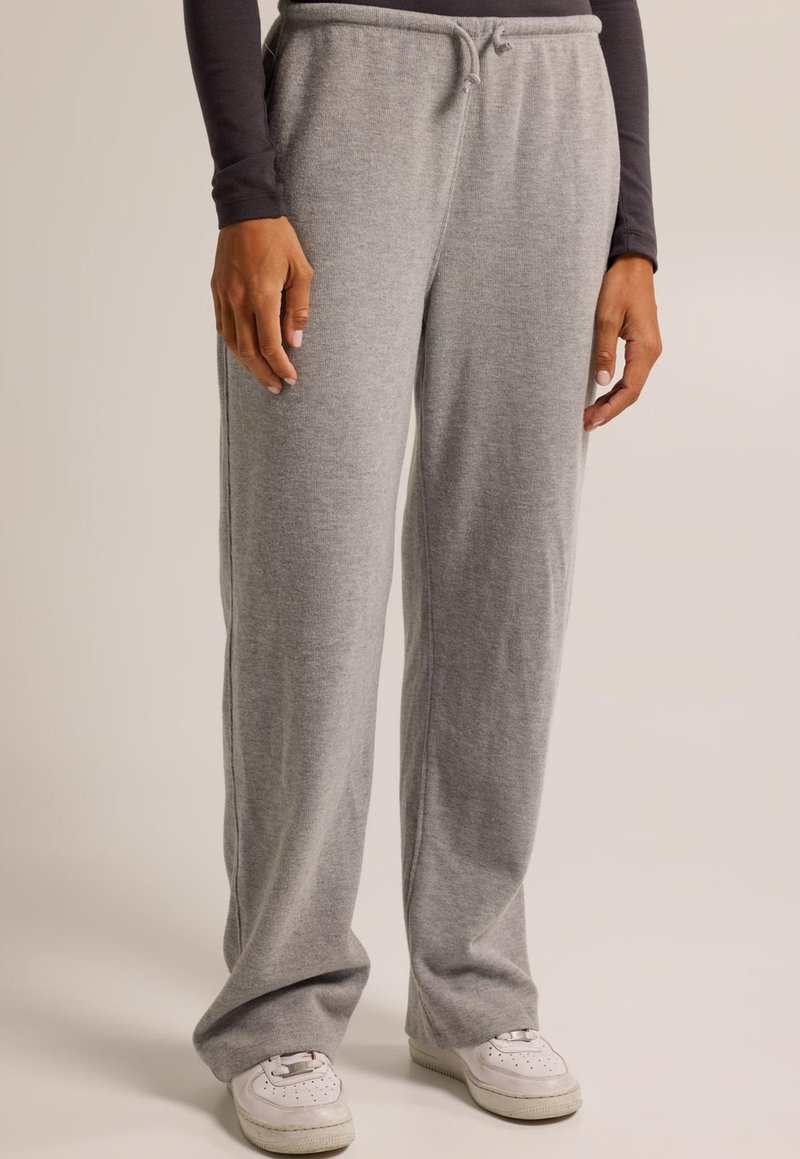 Pantalons de survêtement gris clair avec un cordon de serrage à la taille, design à jambes droites, texture douce et ajustement confortable. Associés à des baskets blanches.