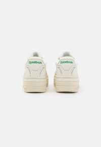 Bele usnjene superge z zelenim logotipom "Reebok", nizka zasnova, zaobljena oblika, oblazinjen ovratnik in teksturiran gumijast podplat.